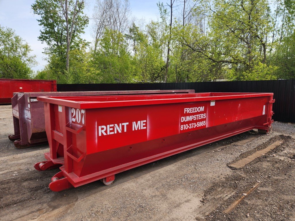 Red Freedom Dumpsters roll-off container with RENT ME and company phone number on a gravel yard